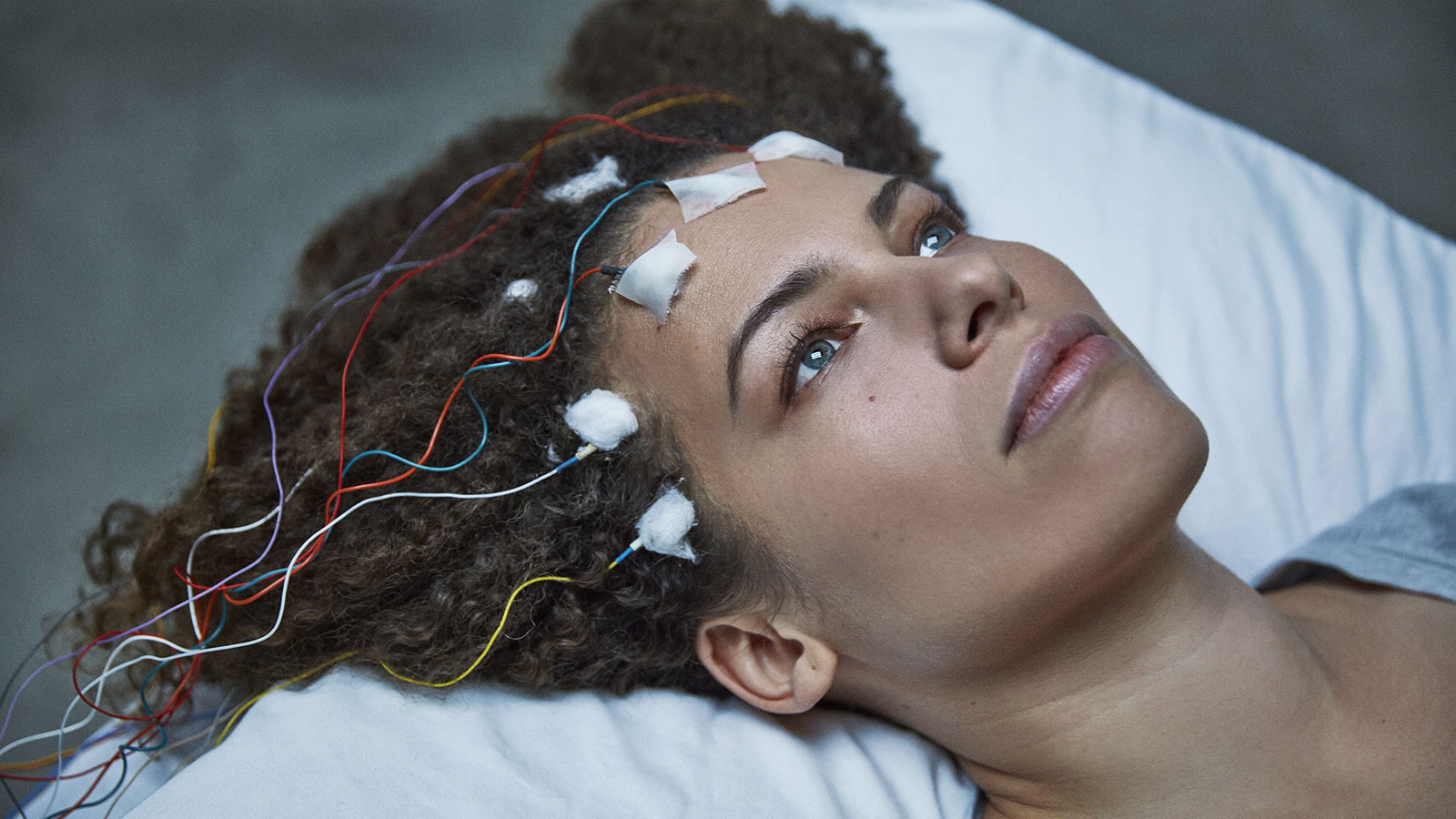 Jennifer Brea is laying on a pillow with probes taped to her forehead and her hairline.